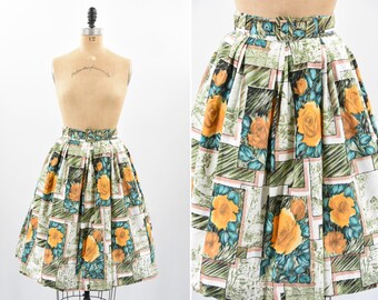 May include: A white, green, and orange floral skirt with a pleated design. The skirt has a geometric pattern with squares and rectangles.