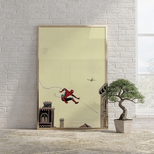 May include: A framed wall art print featuring a red and blue costumed character swinging through the air on a web line above a city skyline. The background is a pale yellow, and a small airplane is visible in the distance above the buildings.