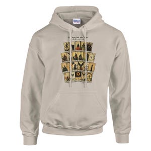 May include: A beige hooded sweatshirt featuring a graphic print of tarot cards arranged in a grid. The text "THE MAJOR ARCANA" is printed above the cards. The hoodie includes a front kangaroo pocket, long sleeves, and a drawstring hood.