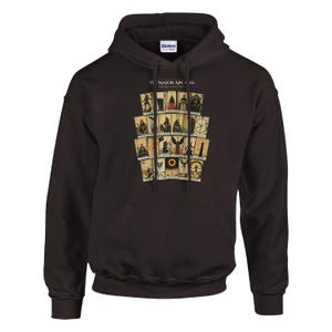May include: A dark brown hooded sweatshirt featuring a graphic print of twenty-two tarot cards arranged in a grid. The text at the top of the graphic reads THE MAJOR ARCANA. The hoodie includes a front kangaroo pocket and matching drawstring cords.