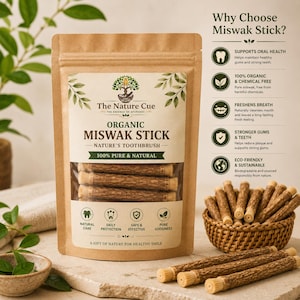 May include: A brown paper pouch labeled Organic Miswak Stick Nature's Toothbrush with a clear window showing wooden sticks. Beside it, a small woven basket holds more sticks, with additional sticks resting on a stone surface nearby.