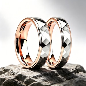 Könnte beinhalten: Zwei Ringe mit einem polierten Innenband aus Roségold und einer facettierten, silberfarbenen Außenfläche mit einem sich wiederholenden rautenförmigen Muster. Die Ringe stehen aufrecht und zeigen den Kontrast zwischen dem metallischen Roségold und Silber.