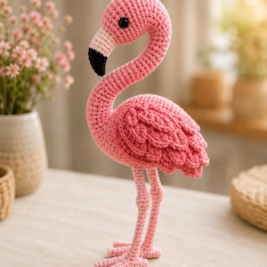 May include: A handcrafted crochet flamingo figurine featuring a vibrant pink body with textured wing details, a long curved neck, and a beak colored in light pink and black. The bird has a single visible black eye and stands on two thin legs.