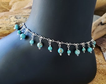 May include: Silver anklet with turquoise beads dangling from the chain. The anklet is on a mannequin's ankle.