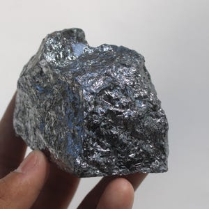 以下が含まれることがあります： 非常に反射率の高いダークグレーの結晶面を持つ、金属シリコンの粗くギザギザした塊。この鉱物標本は、鋭く不規則なエッジと、凹凸のある多面的な脆そうな外観の構造全体に光を捉える、高密度で光沢のある質感が特徴です。
