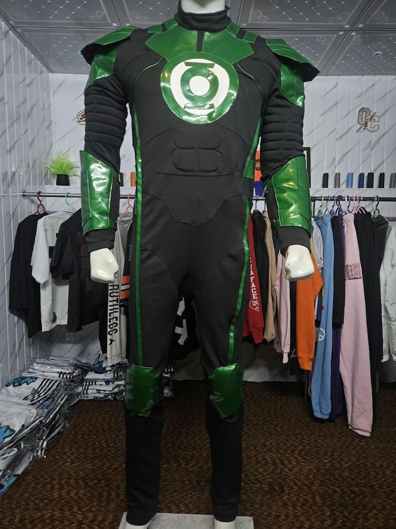 Puede incluir: Un disfraz de cuerpo completo de Green Lantern que presenta un mono negro con detalles verdes en hombros, antebrazos y rodillas. El pecho muestra un emblema circular verde y blanco. El traje incluye secciones acolchadas en el torso.
