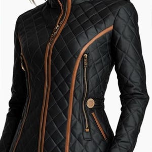 May include: A black quilted jacket featuring a high collar and tan leather-like trim along the front zipper, pockets, and seams. The jacket includes gold-toned hardware, including a central zipper, vertical side zippers, and a circular button detail.