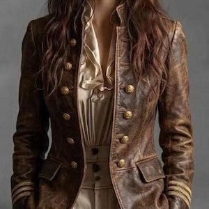 May include: A distressed brown leather jacket featuring a high collar, long sleeves with gold-toned cuff detailing, and two rows of gold-toned buttons down the front. The jacket is worn over a light beige blouse with a ruffled neckline and high-waisted trousers.