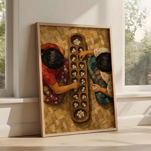 May include: A framed wall art print depicting two individuals playing a traditional mancala board game with cowrie shells. The scene shows a wooden board with multiple circular indentations filled with white shells, set against a woven mat background.