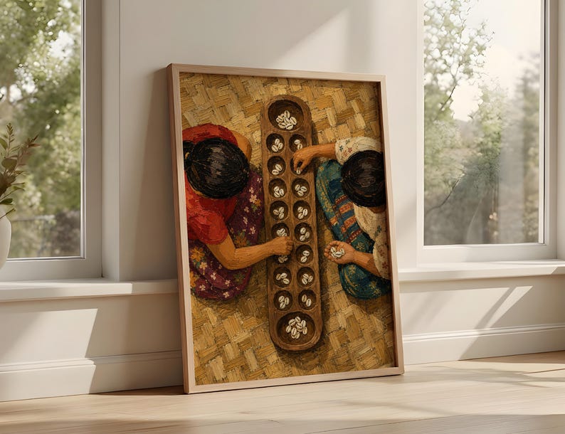 May include: A framed wall art print depicting two individuals playing a traditional mancala board game with cowrie shells. The scene shows a wooden board with multiple circular indentations filled with white shells, set against a woven mat background.