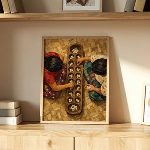 May include: A framed wall art print depicting two individuals playing a traditional mancala board game with small white shells. The wooden board features two rows of circular pits, and the scene is captured from a top-down perspective.
