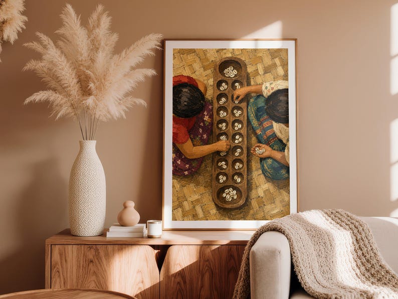 May include: A framed wall art print depicting two individuals playing a traditional board game with small white shells on a wooden board. The scene shows a top-down view of the players, their colorful clothing, and the textured woven mat surface.