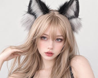 Puede incluir: Una diadema con dos orejas de animal puntiagudas y erguidas hechas de piel sintética negra y gris. Las orejas tienen un borde exterior negro oscuro y un interior gris claro y esponjoso, unidas a una banda fina y flexible para la cabeza.