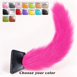 May include: A bright pink faux fur tail attached to a black rectangular leather-like base. Above the tail is a color chart with labels including Pink, Gray, Baby Pink, Orange, Green, Golden, Soft Golden, Black, White, Red, Purple, Yellow, Blue, Dark Brown, Forest Green, and Brown. The text "Choose your color" is printed below.