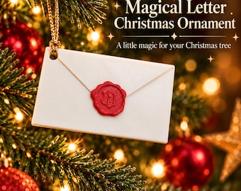 May include: A white envelope-shaped Christmas ornament hanging from a gold string. The ornament features a red wax seal with a crest design. Text on the image reads: Magical Letter Christmas Ornament, A little magic for your Christmas tree.