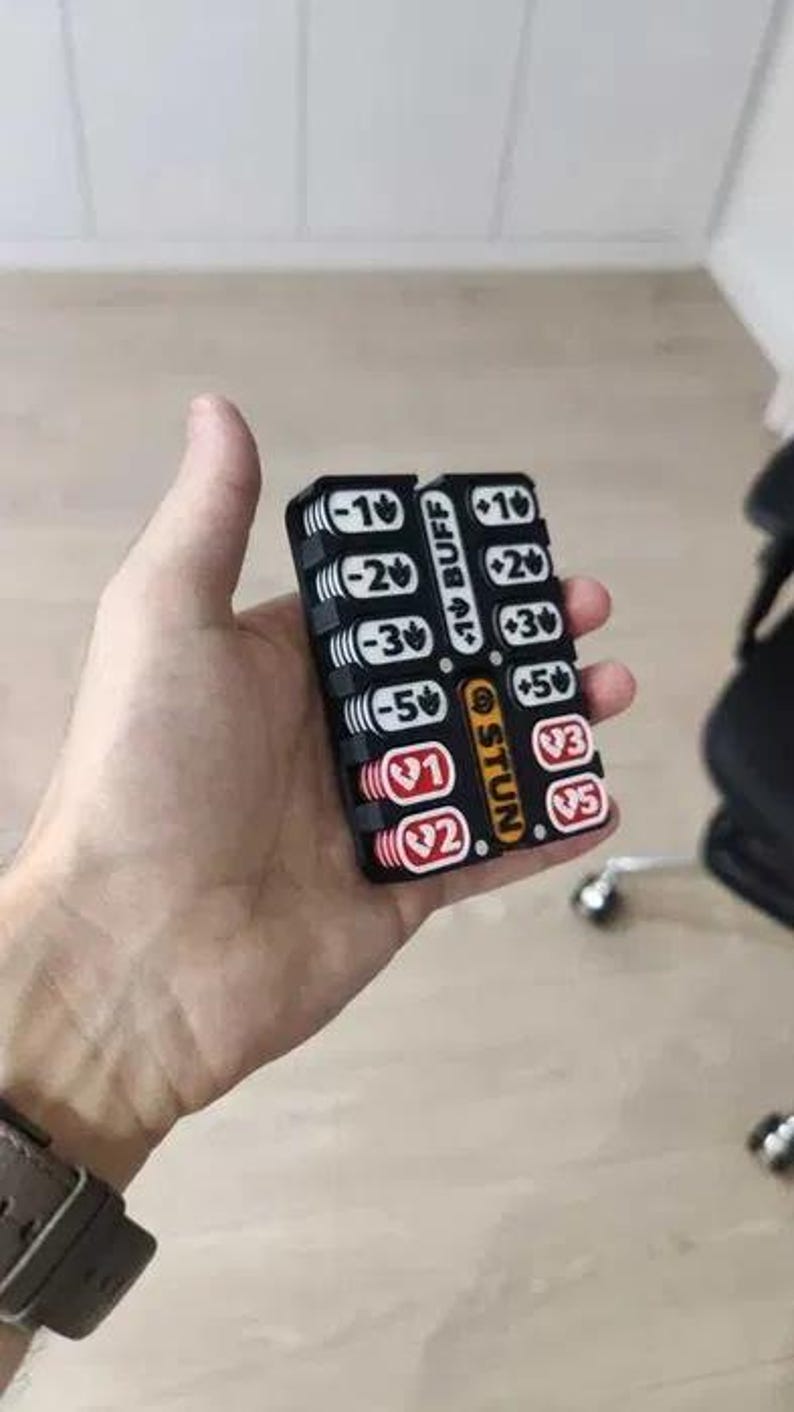 May include: A black plastic game tracker with two columns of sliding numbered tokens. The left column features white tokens with negative values and red tokens with heart icons. The right column has white tokens with positive values and red heart icons.