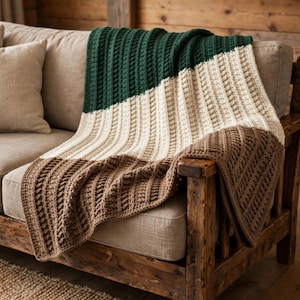 May include: A color-blocked crochet throw blanket featuring three distinct horizontal sections in dark forest green, cream, and light brown. The blanket has a textured, vertical ribbed pattern throughout its entire length.