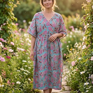 May include: A midi-length kaftan dress in a light blue color featuring a repeating pattern of pink pineapple-like shapes and dark red foliage. The garment has a V-neckline, short wide sleeves, and a drawstring waist tie for an adjustable fit.