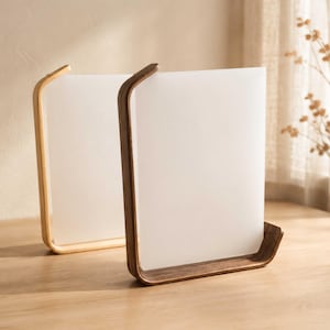 May include: Two rectangular table lamps featuring smooth, curved wooden frames. One lamp has a light-toned wood base, while the other has a dark-toned wood base. Both lamps contain a flat, opaque white panel that diffuses light evenly across the surface.