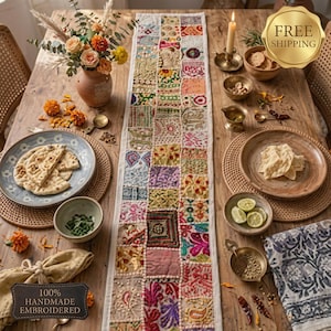 May include: A long rectangular table runner featuring a patchwork design of various embroidered fabric squares in multiple colors, including pink, green, yellow, and blue, with metallic thread accents and small mirrors on a wooden dining table.