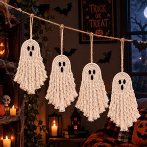 May include: Four off-white macrame ghost ornaments hanging from a jute twine string. Each ghost features a rounded head with two black felt eyes and a black felt mouth, with long, frayed cord fringe forming the body and a loop for hanging.