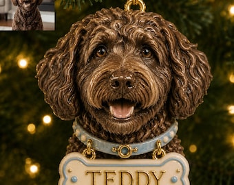 May include: A brown curly-haired dog ornament with a light blue collar and a bone-shaped name tag that reads TEDDY in gold lettering. The ornament features a detailed sculpted face with dark eyes and an open mouth showing a pink tongue.