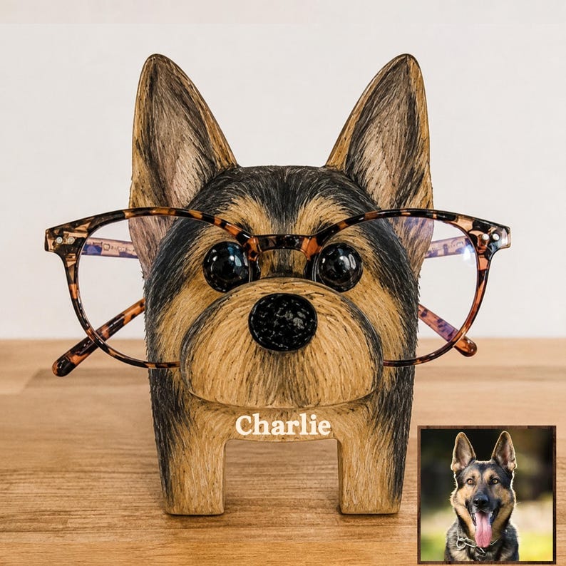 May include: A wooden eyeglass holder shaped like a German Shepherd dog head with black and tan painted fur details. The holder features the name Charlie printed in white text on the front and supports a pair of brown tortoiseshell glasses.