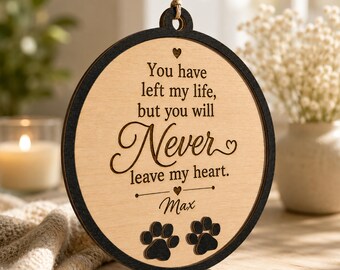 Puede incluir: Un adorno conmemorativo redondo de madera con borde negro y centro de madera clara. Presenta el texto grabado: You have left my life, but you will Never leave my heart. El nombre Max está grabado debajo, flanqueado por dos huellas de pata.