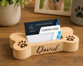 May include: A light-colored wooden business card holder shaped like a dog bone, featuring two dark brown paw print engravings on the ends and the name David engraved in script on the front, holding a card with the text Company Name.