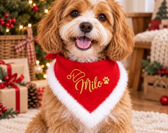 May include: A tan and white dog wearing a red triangular bandana with white faux fur trim. The bandana features gold embroidered text that reads Milo, accompanied by a small gold Santa hat icon and a gold paw print graphic.