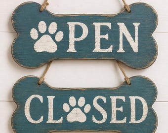 May include: Two bone-shaped wooden signs with a distressed teal finish and white lettering. The top sign features a paw print and the word OPEN, while the bottom sign displays a paw print and the word CLOSED. Both signs hang from jute twine.