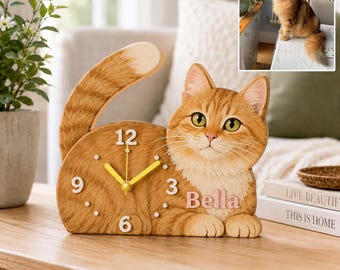 May include: A wooden desk clock shaped like a ginger tabby cat with a long curved tail. The clock face features white numbers 3, 6, 9, and 12, yellow hands, and the name Bella in pink lettering. The cat has green eyes and a light-colored chest.