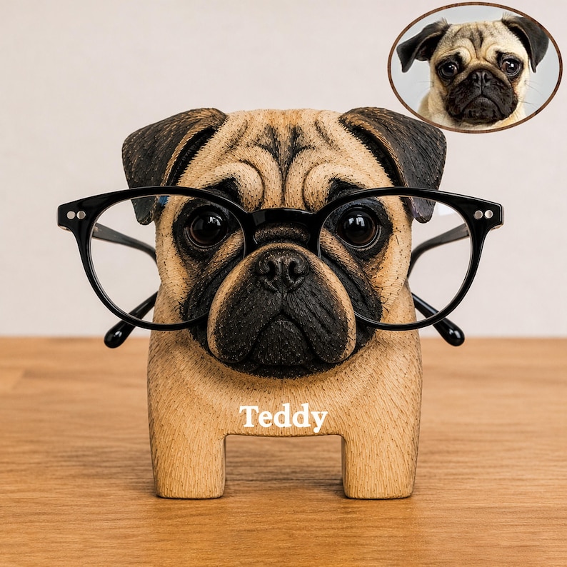 May include: A tan and black pug-shaped eyeglass holder with a black nose and ears. The figure features the name Teddy printed in white on the front. A pair of black-rimmed glasses rests on the pug's face. A small circular inset shows a real pug.