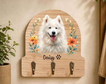 May include: A light wood wall-mounted hook rack with an arched top, featuring a printed illustration of a white Samoyed dog surrounded by orange and yellow flowers. The name Daisy and a paw print are printed below the dog, with three metal hooks.