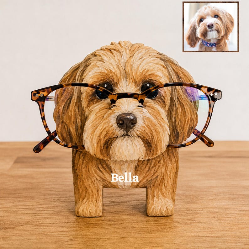 May include: A brown dog-shaped eyeglass holder with textured fur details, featuring the name Bella printed in white on the chest. The figurine is wearing a pair of brown tortoiseshell-patterned glasses across its face.
