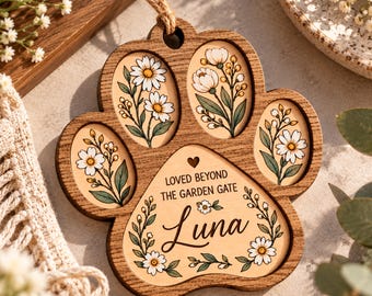 May include: A wooden paw-shaped ornament featuring four oval insets with floral illustrations and a central section engraved with the text "LOVED BEYOND THE GARDEN GATE" and the name "Luna" surrounded by delicate flower and leaf designs.