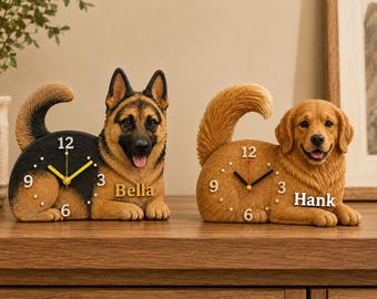 Puede incluir: Dos relojes analógicos con forma de perro. El reloj de la izquierda es un pastor alemán negro y fuego con el nombre Bella impreso en el lateral. El reloj de la derecha es un golden retriever marrón dorado con el nombre Hank impreso en el lateral. Ambos relojes tienen los números blancos 3, 6, 9 y 12 en sus cuerpos.