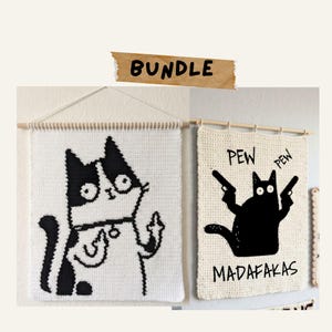 Puede incluir: Un conjunto de dos tapices de ganchillo rectangulares sobre varillas de madera. La pieza de la izquierda muestra un gato blanco y negro haciendo una peineta. La pieza de la derecha muestra un gato negro con dos pistolas y el texto PEW PEW MADAFAKAS.