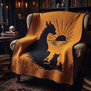 Puede incluir: Una manta de ganchillo rectangular con fondo amarillo mostaza, que presenta la silueta negra de un dragón y una criatura más pequeña sentadas juntas frente a un diseño de sol negro que se refleja sobre una línea de horizonte.