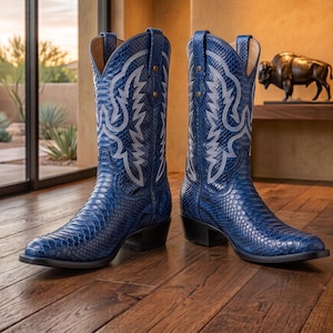 Puede incluir: Un par de botas vaqueras azules con un patrón texturizado de piel de serpiente, puntera puntiaguda y tacón de bloque. La caña de cada bota está decorada con intrincadas costuras blancas en forma de ala, con dos tiradores en el borde superior.