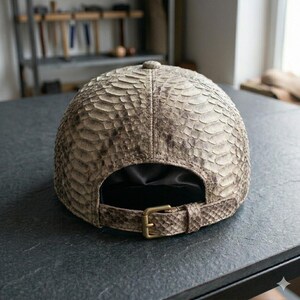 Pu&ograve; includere: Un cappellino da baseball realizzato in pelle di serpente testurizzata nei toni del beige e del grigio. Il cappellino presenta una struttura a sei pannelli con un bottone centrale sulla corona e un cinturino posteriore regolabile con fibbia in ottone.