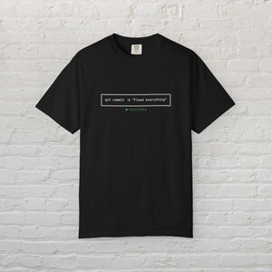 Może przedstawiać: Czarny t-shirt z krótkim rękawem z białą prostokątną grafiką zawierającą tekst git commit -m "Fixed everything", po którym następuje zielona kropka i słowo SUCCESS napisane zielonymi wielkimi literami, wyśrodkowane na klatce piersiowej.