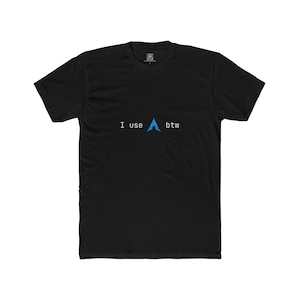 May include: A black short-sleeved t-shirt featuring the white text "I use" followed by a blue Arch Linux logo and the white text "btw" centred on the chest. The shirt has a crew neckline and a standard fit, with a small brand label visible inside the collar.