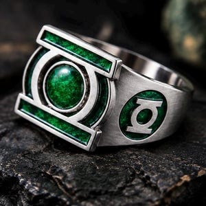 May include: A silver-toned metal ring featuring the Green Lantern emblem. The centerpiece is a circular, metallic green inlay surrounded by a rectangular frame with green accents. A smaller circular green inlay with the logo is on the side.