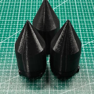 Peut inclure: Trois objets noirs en forme de cône avec une base cylindrique et un sommet pointu. Chaque objet présente une texture imprimée en 3D visible avec des lignes de couche verticales le long de la surface et de petites saillies à la base.