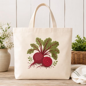 Peut inclure: Un sac fourre-tout en toile couleur crème orné d'une broderie représentant une betterave entière et une betterave coupée avec des feuilles vertes aux nervures rouges. Le motif est centré sur le devant du sac, doté de deux anses solides.