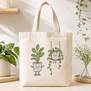 Può includere: Una borsa tote in tela color crema con un'illustrazione grafica di due piante in vaso antropomorfe. Una pianta è in piedi sul terreno, mentre l'altra è seduta su un'altalena di legno. Entrambe le piante hanno volti sorridenti e arti sottili.