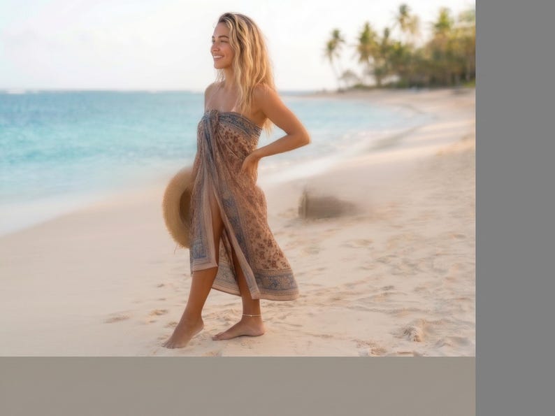 Puede incluir: Un pareo sin tirantes con un estampado floral en tonos marr&oacute;n y azul con un borde decorativo. La tela ligera est&aacute; envuelta alrededor del torso y las piernas, creando una silueta fluida. Se sostiene un sombrero de paja de ala ancha a un lado.