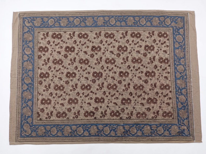 Puede incluir: Un textil rectangular que presenta un campo central de patrones florales marrones sobre un fondo beige claro, encerrado por un borde ancho de motivos florales azules y marrones. La tela muestra un dise&ntilde;o de estampado en bloque.