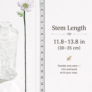 May include: A glass flower with translucent white and purple petals, a yellow center, and a green leaf on a thin, flexible wire stem. A measuring tape shows a stem length of 11.8 to 13.8 inches. Text reads: Stem Length 11.8&ndash;13.8 in (30&ndash;35 cm).